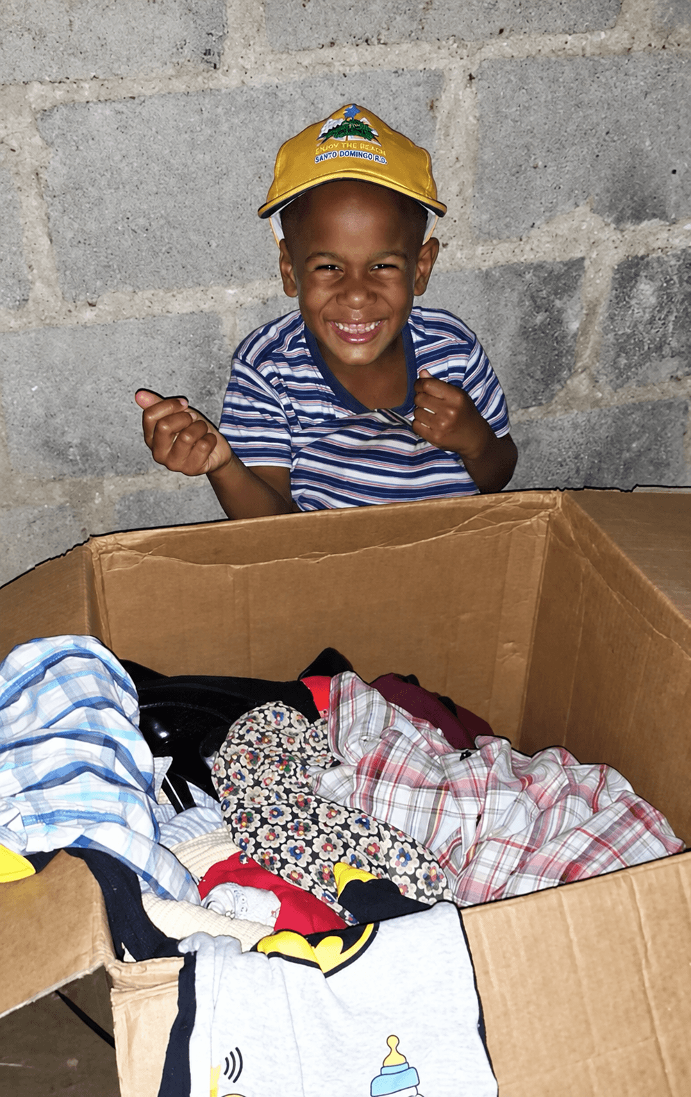 A smiling boy in a yellow hat opening a box of donated clothing